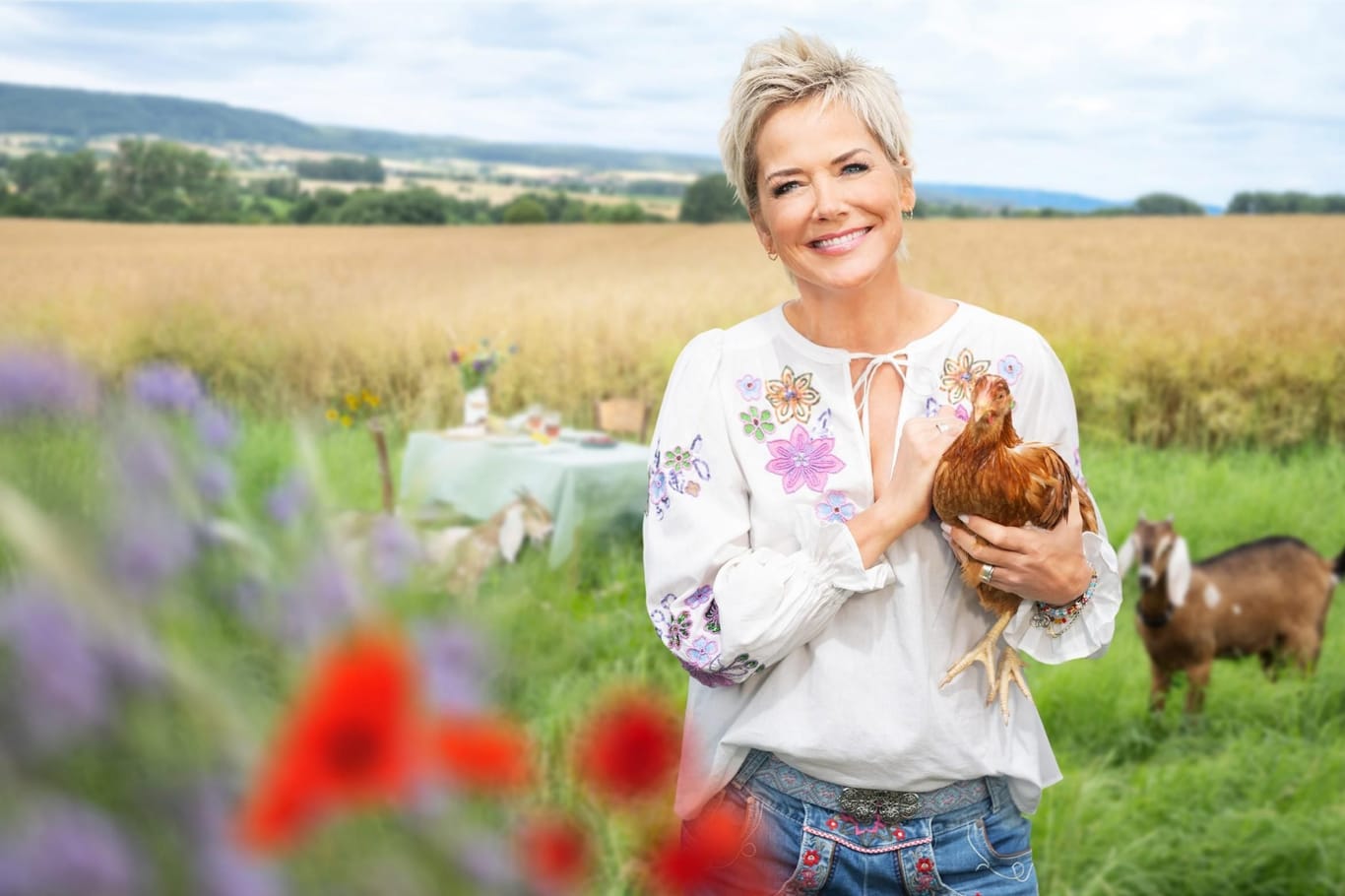 "Bauer sucht Frau"-Moderatorin Inka Bause steht auf einem Feld und hält ein Huhn.