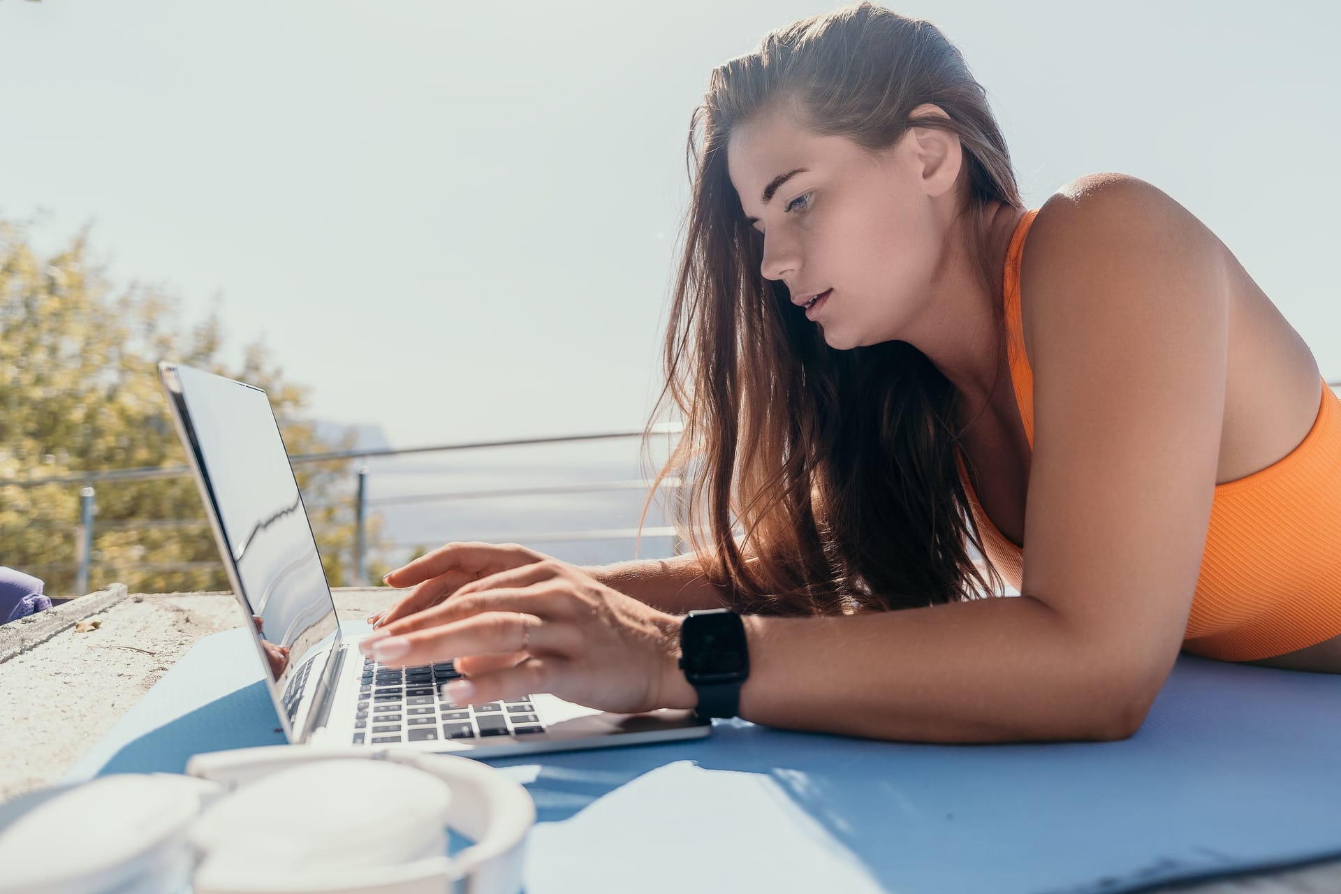 Eine Frau liegt am Strand und arbeitet am Laptop (Symbolbild): Das Konzept "Workation" verbindet den Job mit Urlaub.