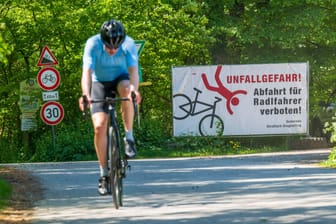 Ein Radfahrer fährt bei Straßlach-Dingharting an einem Schild mit der Aufschrift "Unfallgefahr – Abfahrt für Radfahrer verboten!" vorbei.