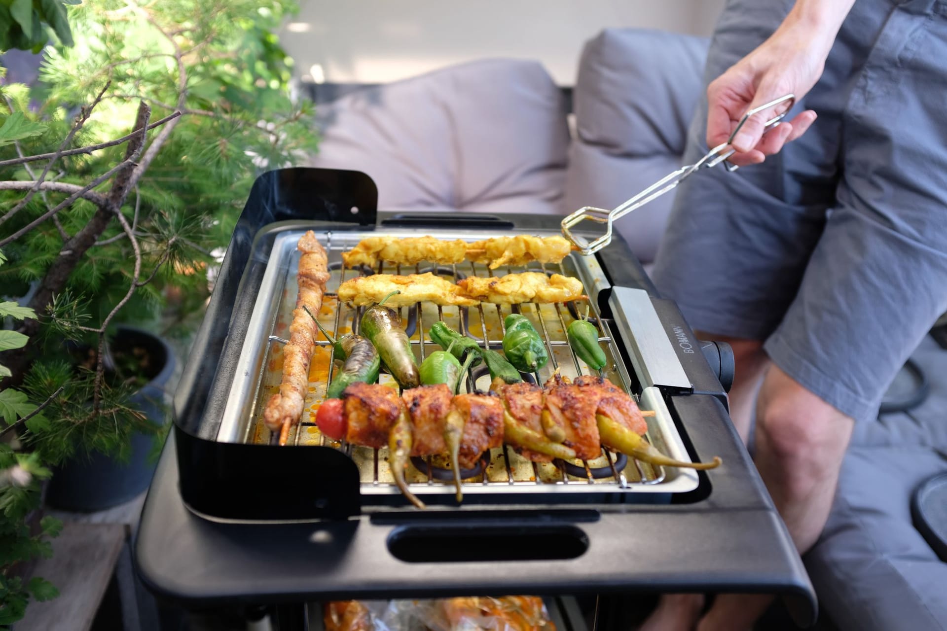 Ein Mann grillt mit einem Elektrogrill auf einem Balkon