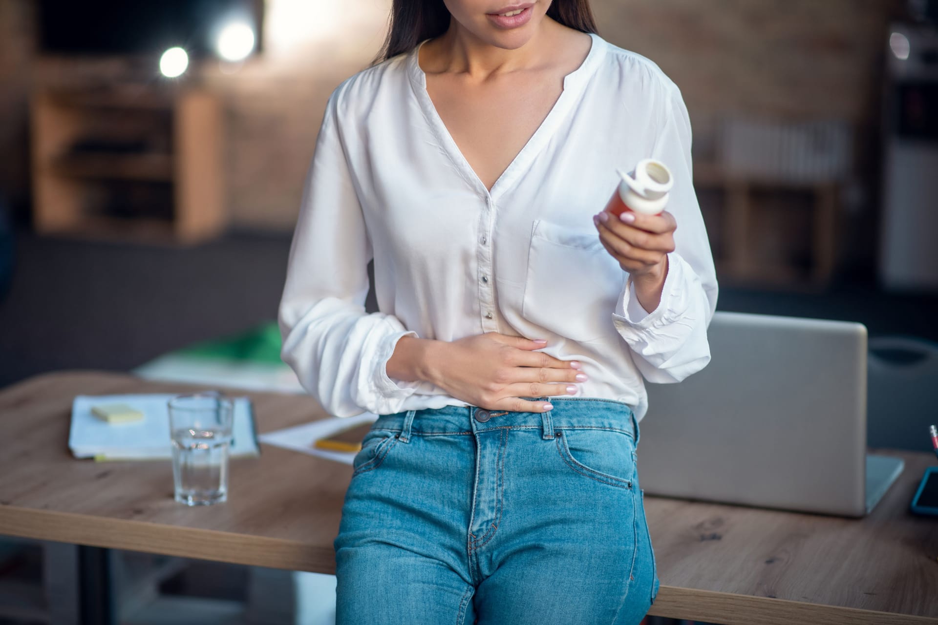 Frau mit einer Dose Tabletten in der Hand hält sich den Bauch