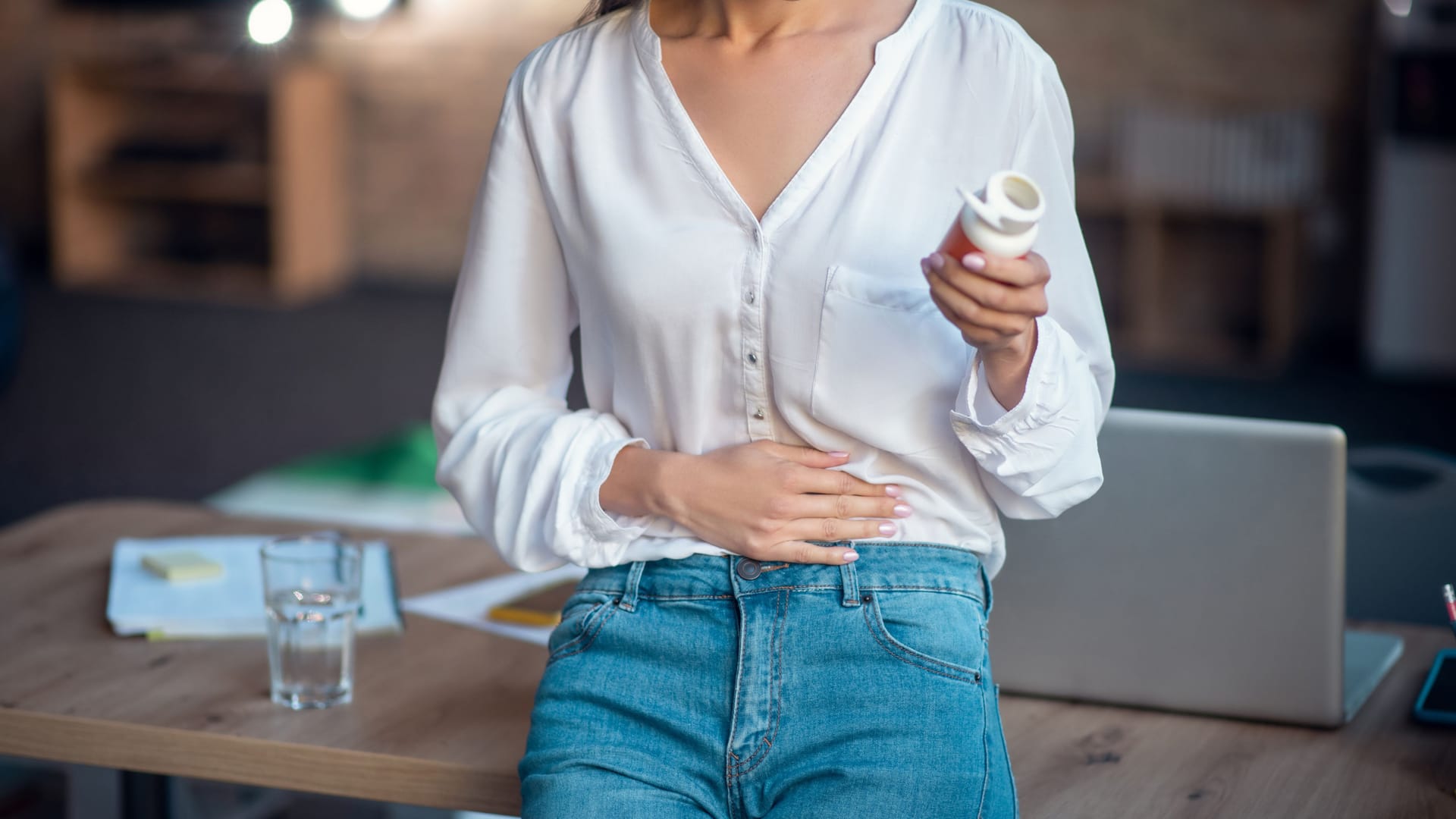 Frau mit einer Dose Tabletten in der Hand hält sich den Bauch