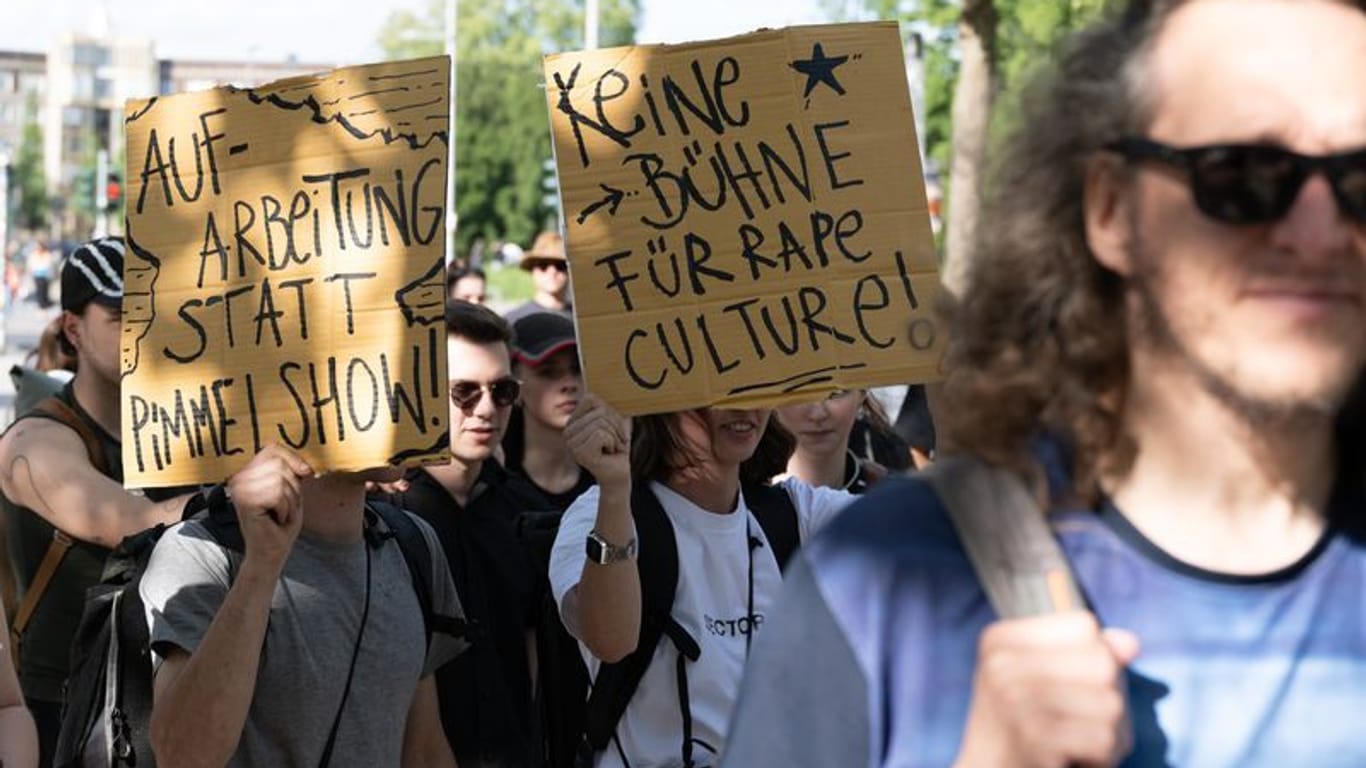 Demonstranten stehen anlässlich einer Kundgebung auf dem Jorge-Gomondai-Platz und halten Schilder mit der Aufschrift "Aufarbeitung statt Pimmelshow" und "Keine Bühne für Rape Culture".
