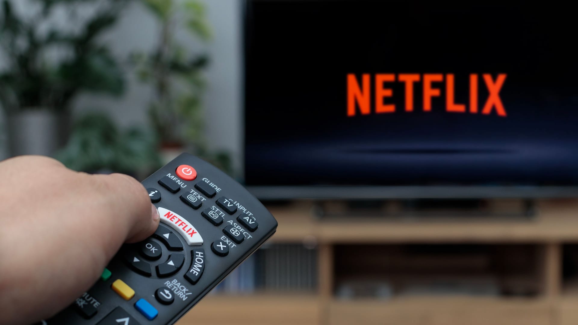 Person holding a TV remote controller displaying the Netflix logo with the Netfl