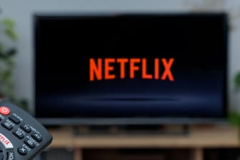 Person holding a TV remote controller displaying the Netflix logo with the Netfl