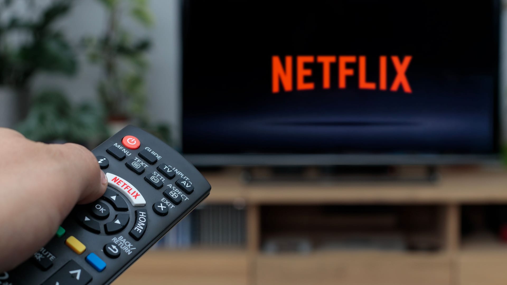 Person holding a TV remote controller displaying the Netflix logo with the Netfl