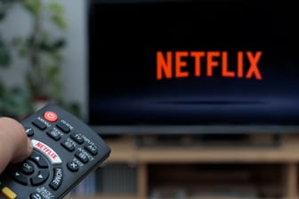 Person holding a TV remote controller displaying the Netflix logo with the Netfl