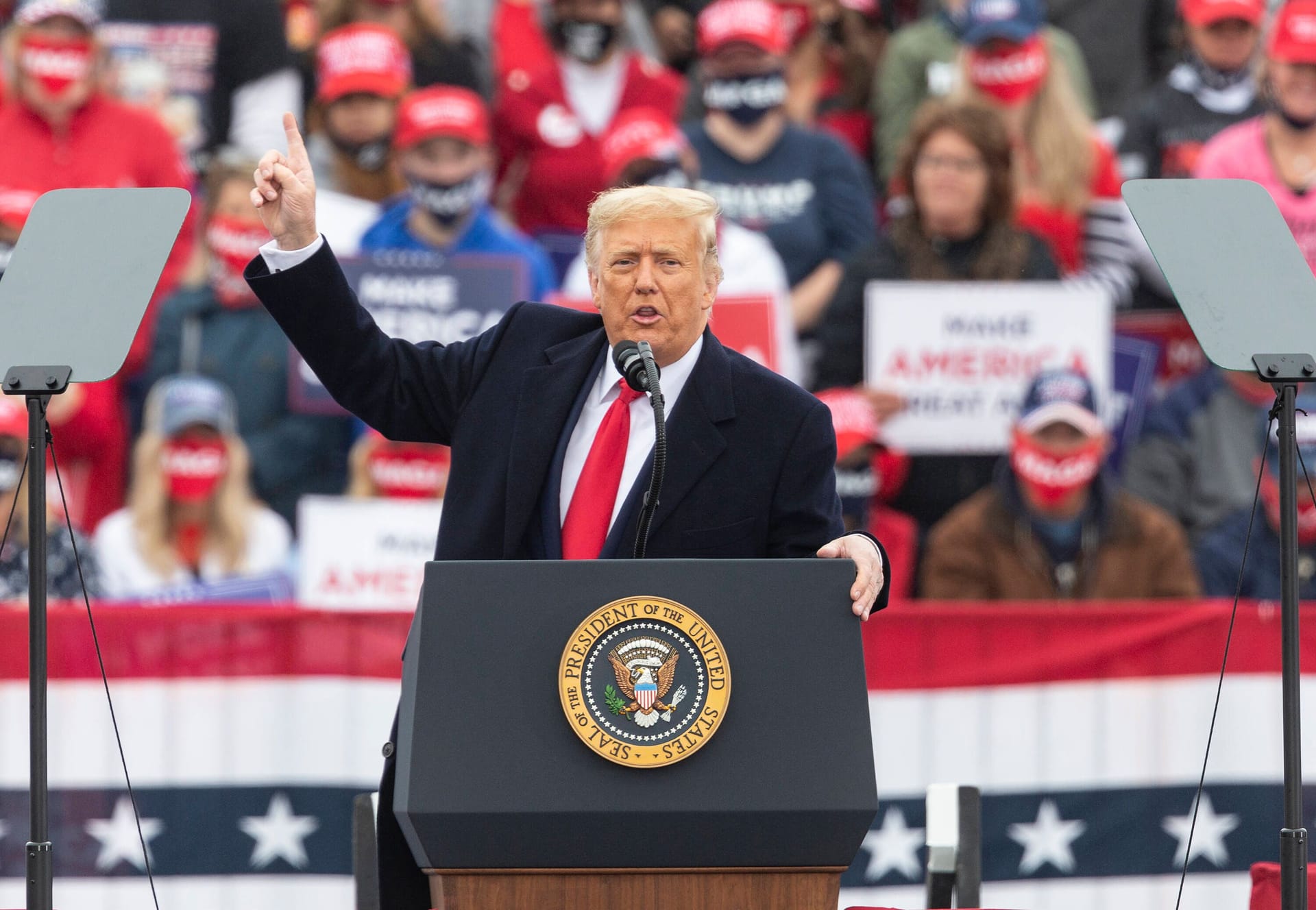 Trump trägt bei Wahlkampfauftritten oft rote Krawatten. Im Hintergrund sind Unterstützer mit roten "Make America Great Again"-Kappen zu sehen.