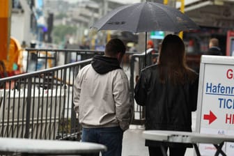 Ein Mann und eine Frau gehen mit einem Regenschirm an den Landungsbrücken entlang (Symbolbild): Eine Starkregenkarte zeigt, wo es in Hamburg gefährlich ist.