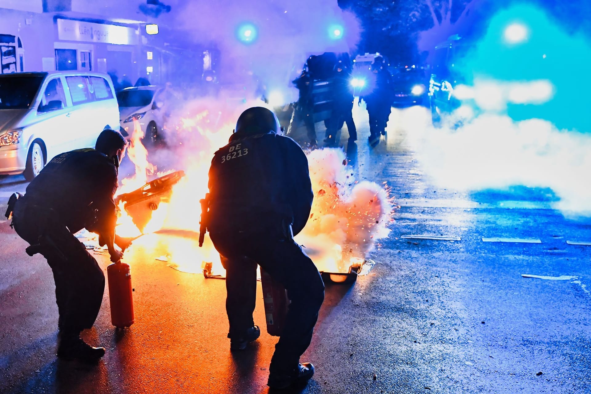 28.05.2024, Berlin: Polizeibeamte versuchen auf der Sonnenallee in Neukölln zwei in Brand gesetzte Mülltonnen zu löschen. In der Sonnenallee kam es zu teilweise gewalttätigen Auseinandersetzungen von Menschen