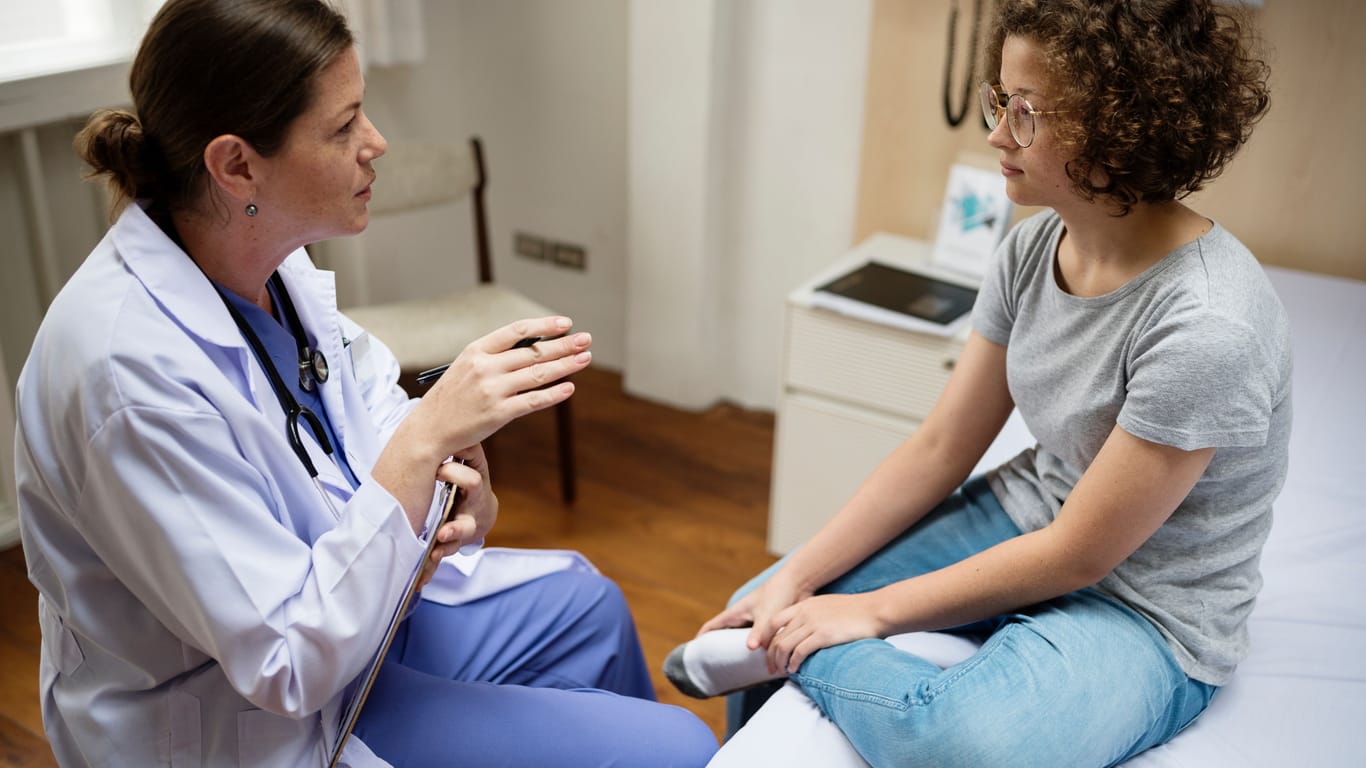 Eine Ärztin spricht mit einer jungen Frau, die sich den linken Fuß hält.