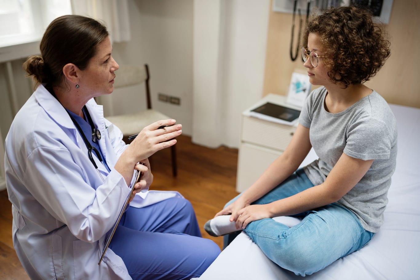 Eine Ärztin spricht mit einer jungen Frau, die sich den linken Fuß hält.