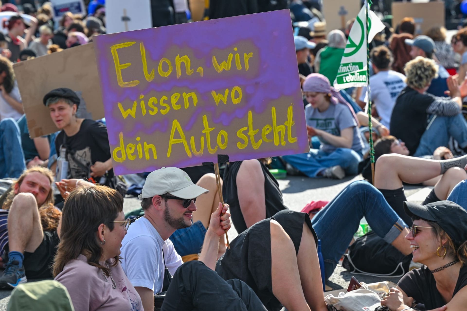 Ein Schild mit der Aufschrift «Elon, wir wissen, wo dein Auto steht» halten Teilnehmer einer Protestveranstaltung vor dem Werk von Tesla in Grünheide in den Händen.