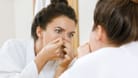 Eine Frau untersucht mit den Fingern etwas an ihrer Nase.
