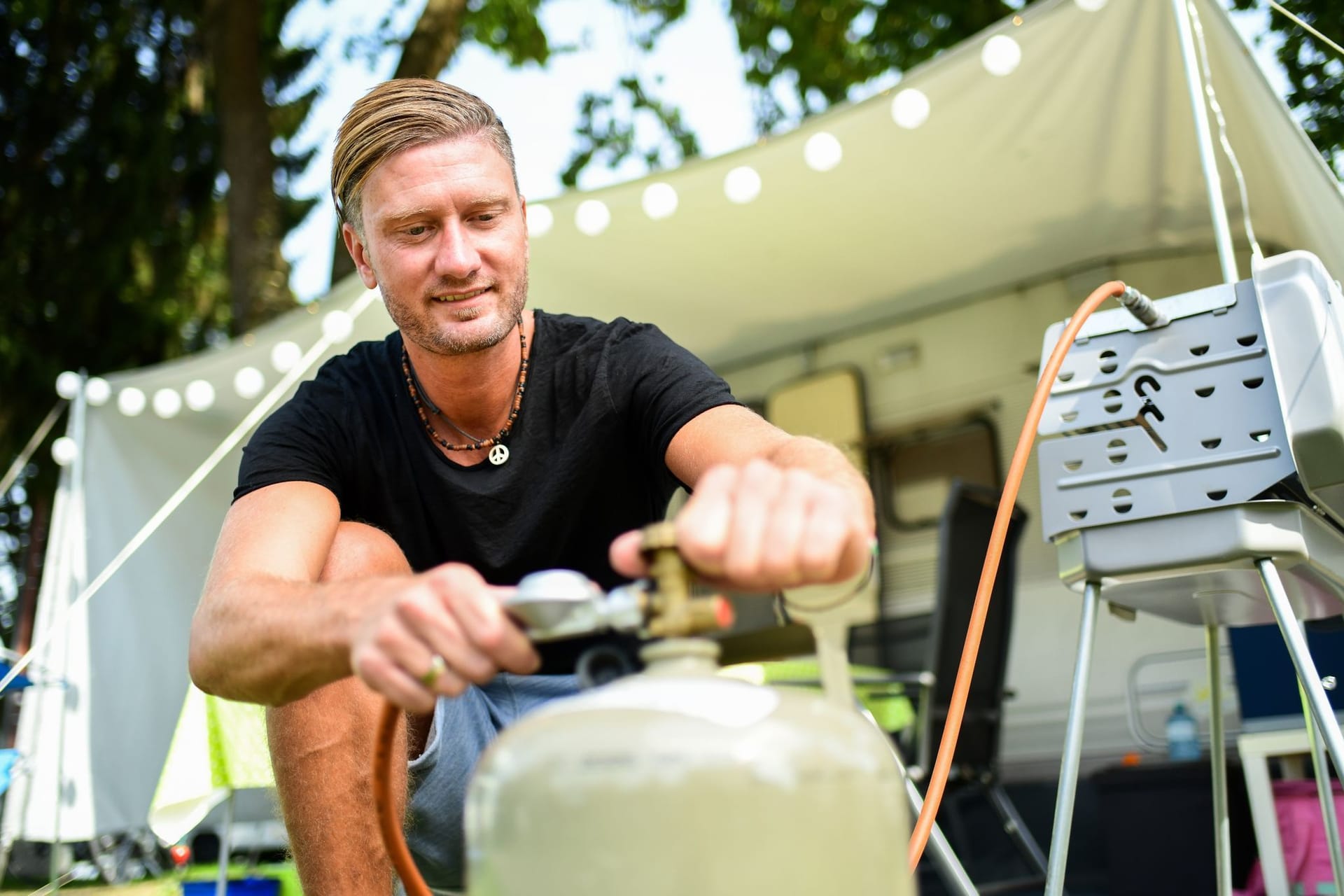 Ein junger Mann schliesst eine Gasflasche an einen Grill an