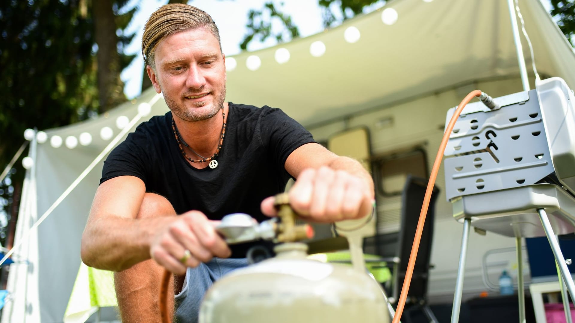 Ein junger Mann schliesst eine Gasflasche an einen Grill an