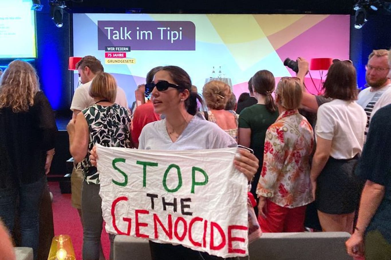 "Stop the Genocide" steht auf einem Transparent, das eine Frau während einer Veranstaltung mit Außenministerin Baerbock im Rahmen der Demokratiefestets anlässlich des Jubiläums 75 Jahre Grundgesetz hält.