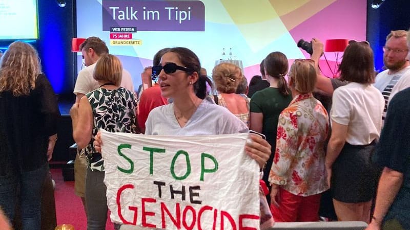 "Stop the Genocide" steht auf einem Transparent, das eine Frau während einer Veranstaltung mit Außenministerin Baerbock im Rahmen der Demokratiefestets anlässlich des Jubiläums 75 Jahre Grundgesetz hält. "Stop the Genocide" steht auf einem Transparent, das eine Frau während einer Veranstaltung mit Außenministerin Baerbock im Rahmen der Demokratiefestets anlässlich des Jubiläums 75 Jahre Grundgesetz hält.