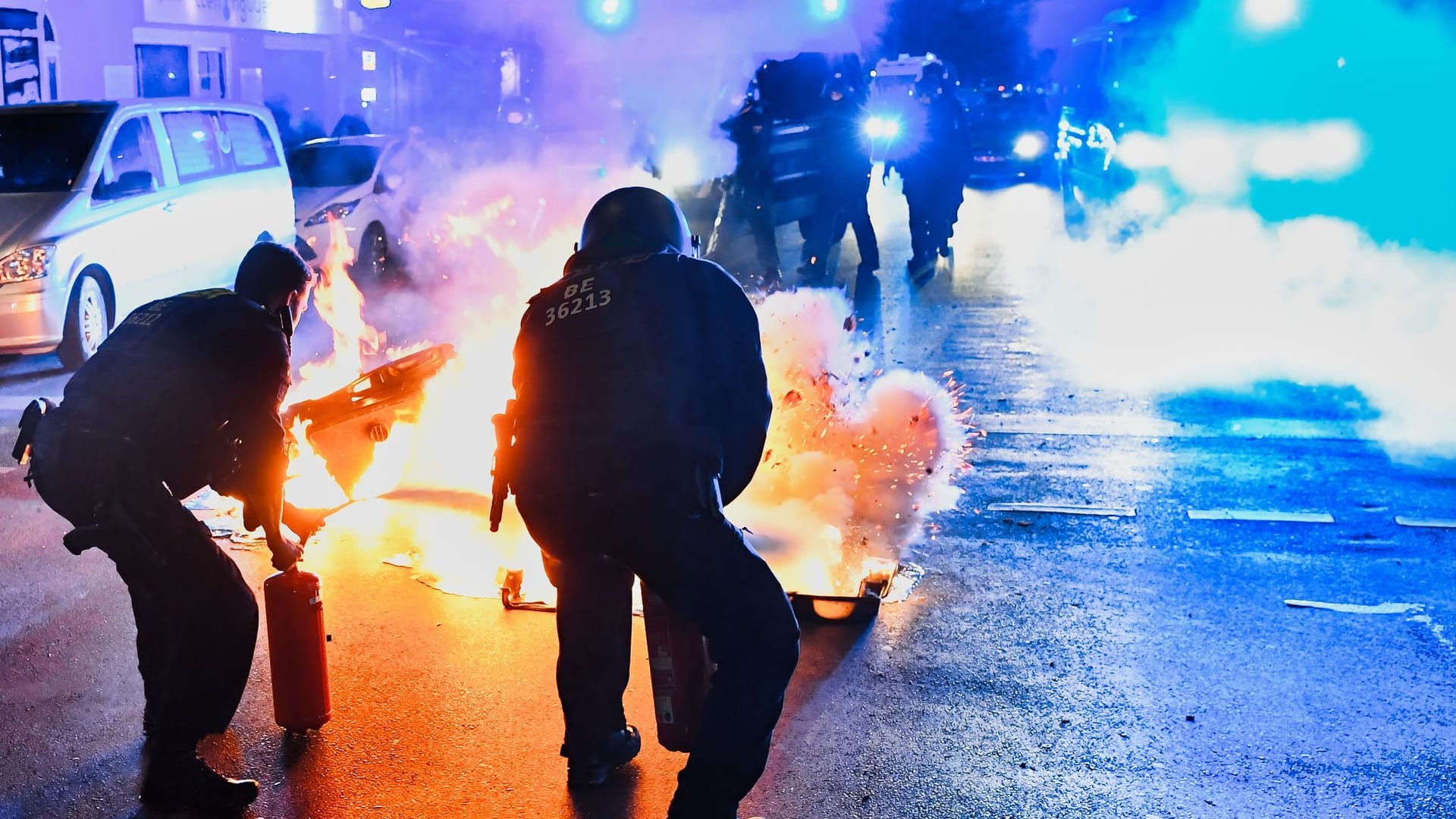 Polizeibeamte versuchen auf der Sonnenallee in Neukölln zwei in Brand gesetzte Mülltonnen zu löschen.