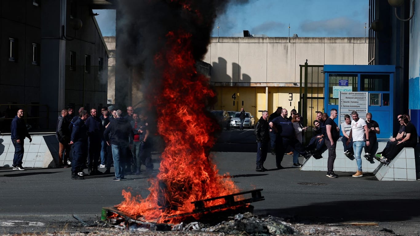 Ein Feuer brennt, während Gefängnispersonal den Eingang des Gefängnisses in Val de Reuil blockiert, in dem der befreite Gefangene inhaftiert war.