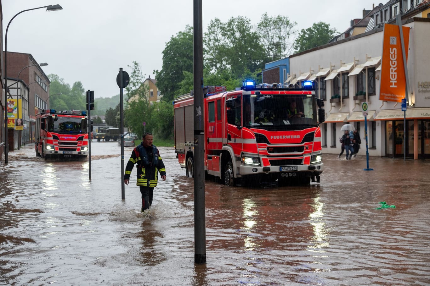 Feuerwehrleute bewegen sich und ihre LKW durch das Hochwasser in der Fischbachstrasse in Saarbrücken.