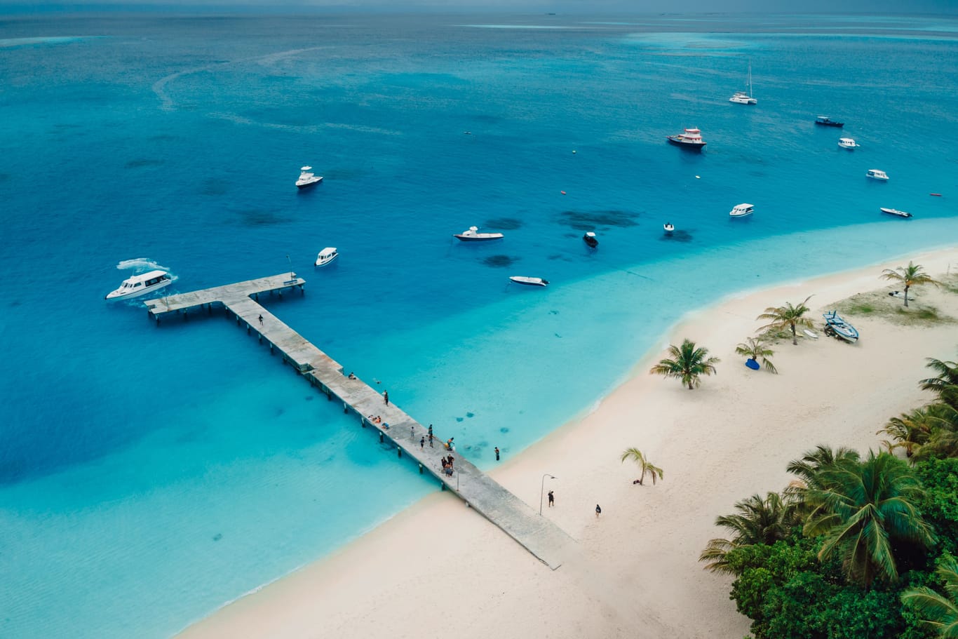 Aerial drone view of paradise Maldives tropical beach with pier and speed boats on island. Summer and travel vacation concept.