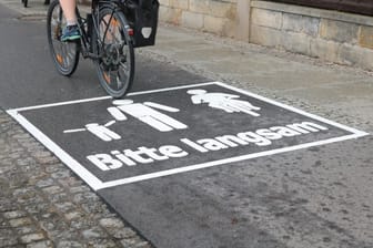 Auf den neuen Warnhinweisen ist ein Radfahrer und ein Elternteil mit Kind zu sehen ist. Darunter steht: "Bitte langsam".