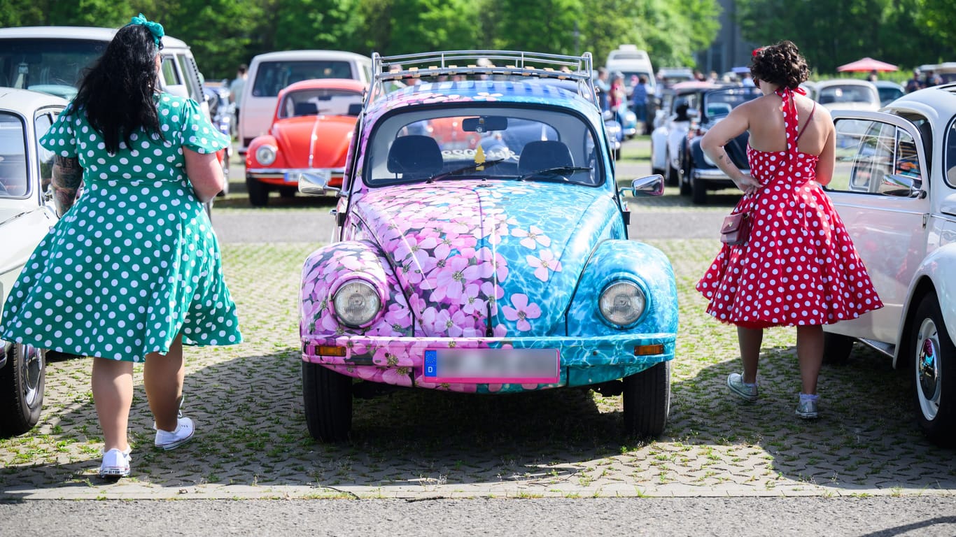 Zwei Frauen in Kleidern laufen neben einem Käfer im Blümchenoptik: Das "Maikäfertreffen" zieht 10.000 Fans an.