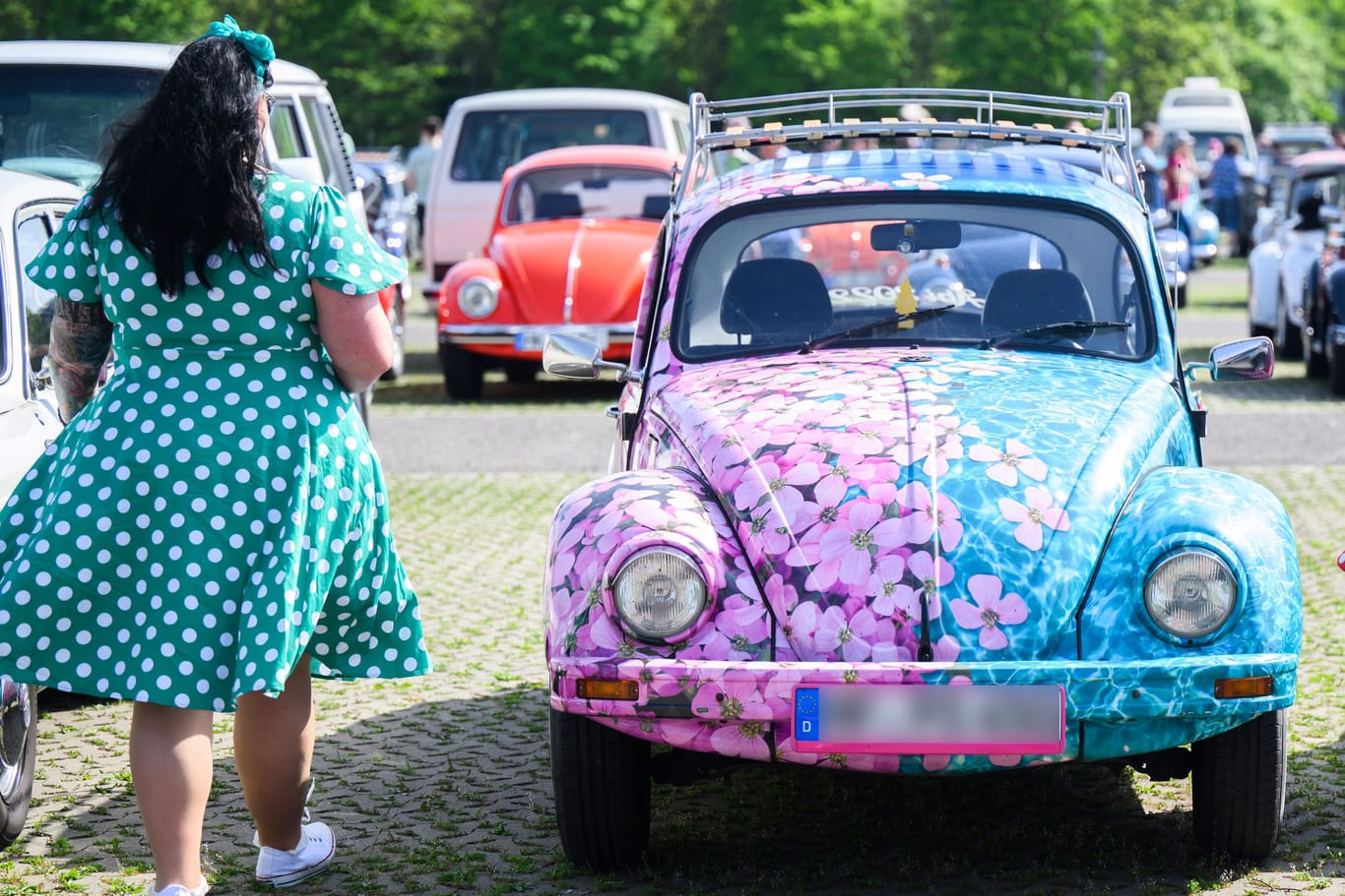 Zwei Frauen in Kleidern laufen neben einem Käfer im Blümchenoptik: Das "Maikäfertreffen" zieht 10.000 Fans an.