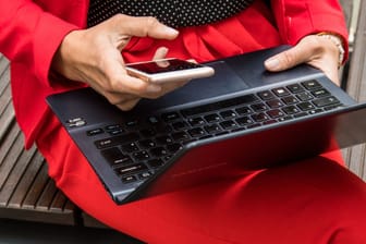 Eine Frau hält ein Smartphone und ein Laptop in den Händen