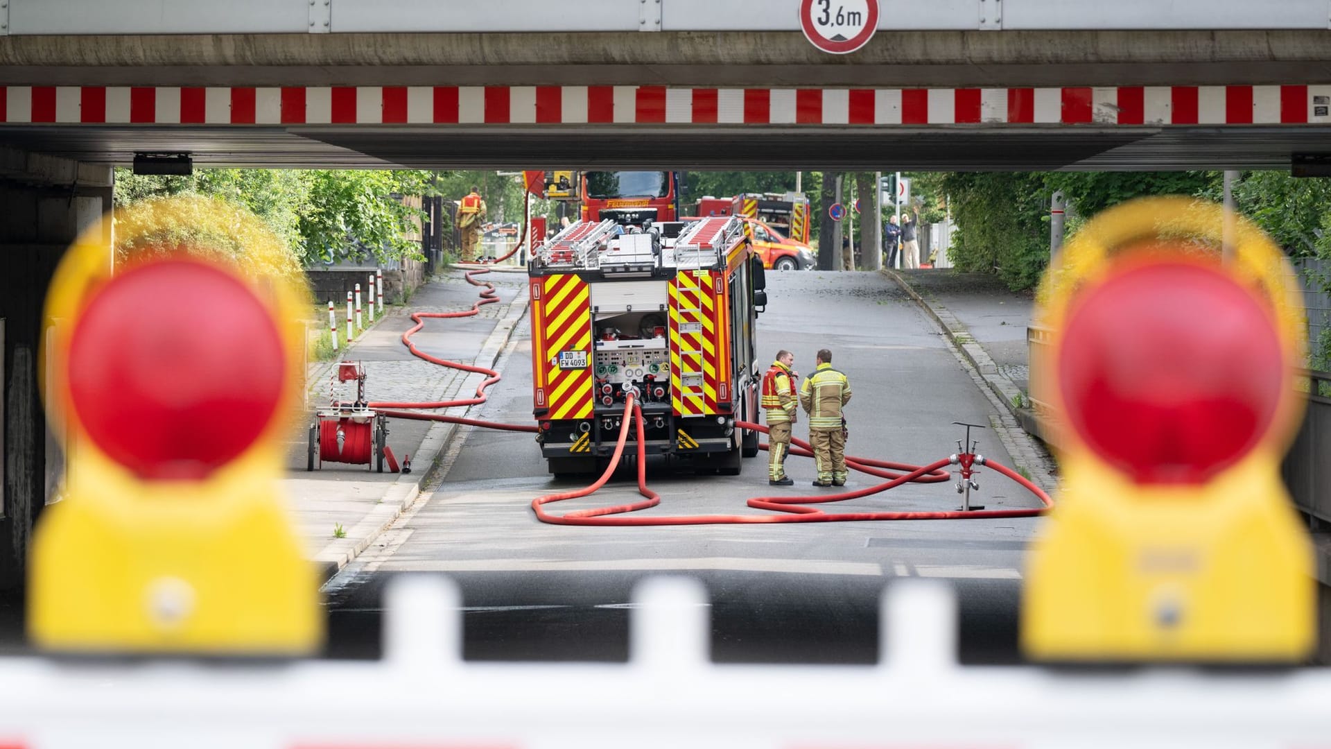 Einsatzkräfte der Feuerwehr sind bei einem Brand in einem Gebäudeteil einer Industriebrache im Dresdner Stadtteil Leuben hinter einer Absperrung zu sehen.