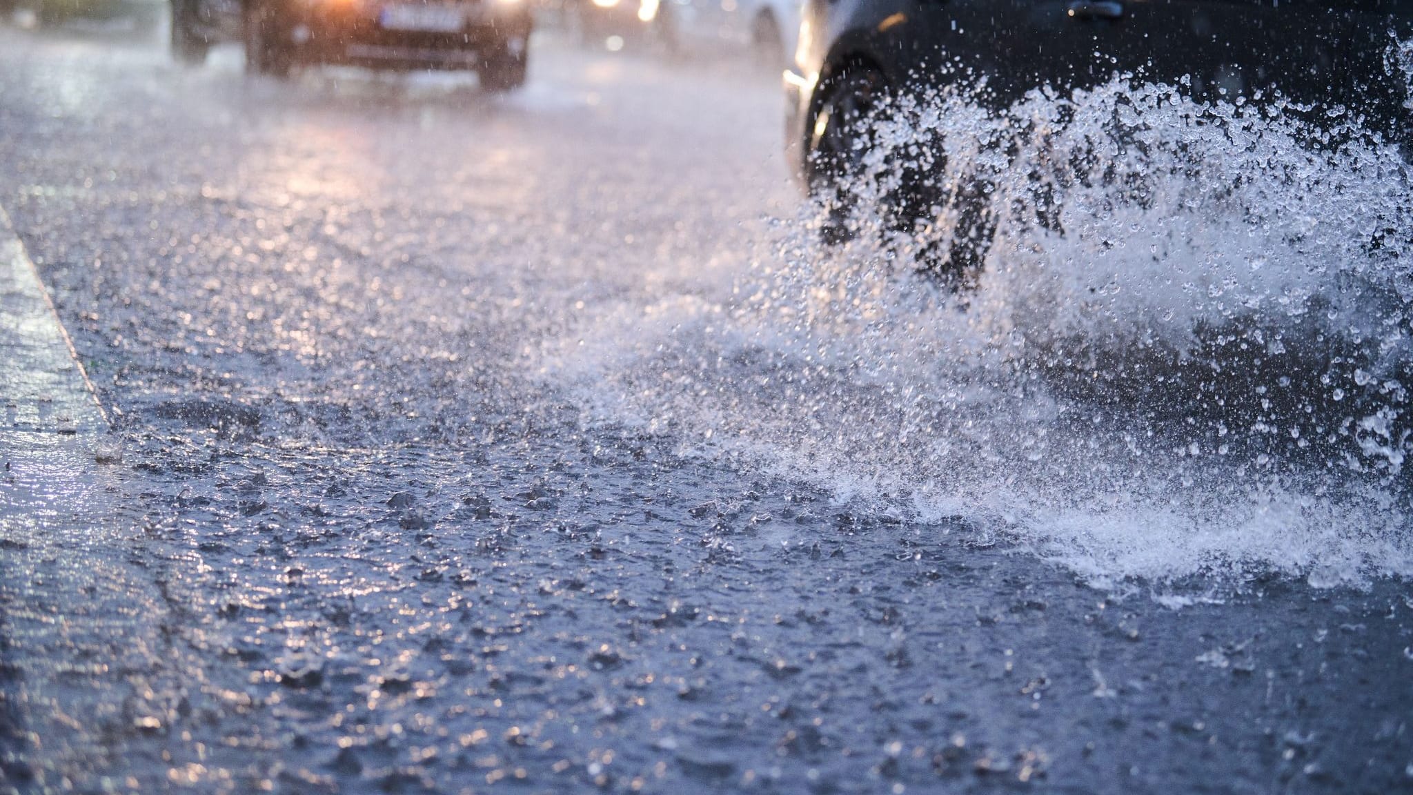 Autos fahren bei starkem Regen durch tiefe Pfützen (Symbolbild): DWD warnt vor Gefahr für Leib und Leben durch Überflutungen von Straßen.