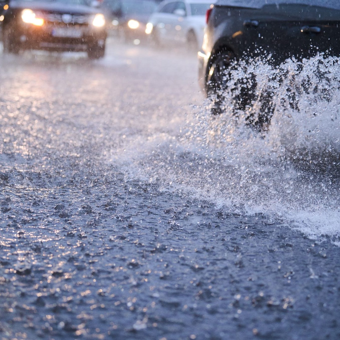 Autos fahren bei starkem Regen durch tiefe Pfützen (Symbolbild): DWD warnt vor Gefahr für Leib und Leben durch Überflutungen von Straßen.