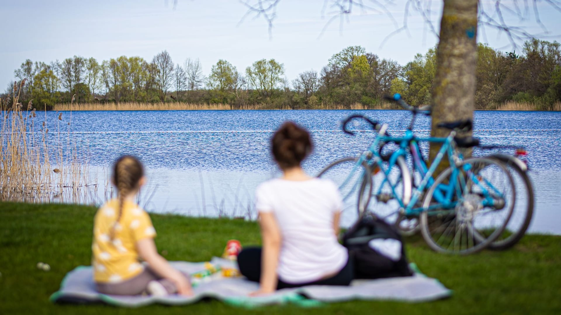 Eine Frau und ein Kind sitzen bei sonnigem Wetter am Ufer des Hufeisensees bei Hannover (Symbolbild): Das Wochenende soll sommerlich werden.