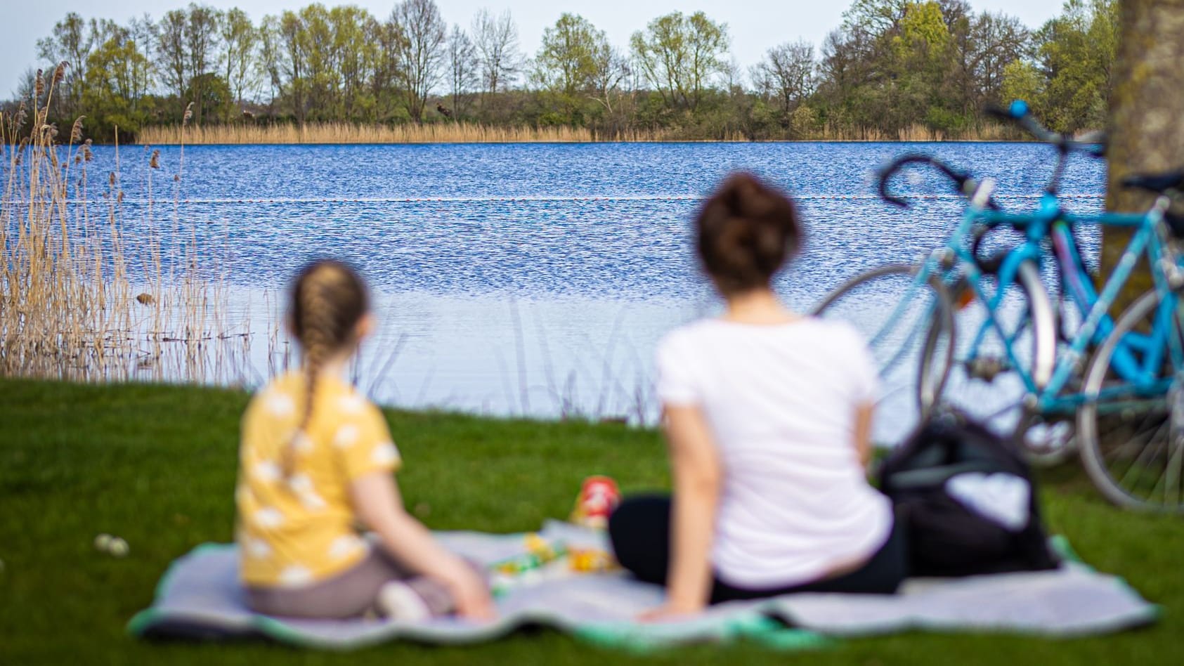 Eine Frau und ein Kind sitzen bei sonnigem Wetter am Ufer des Hufeisensees bei Hannover (Symbolbild): Das Wochenende soll sommerlich werden.