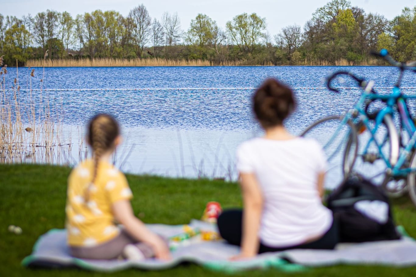 Eine Frau und ein Kind sitzen bei sonnigem Wetter am Ufer des Hufeisensees bei Hannover (Symbolbild): Das Wochenende soll sommerlich werden.