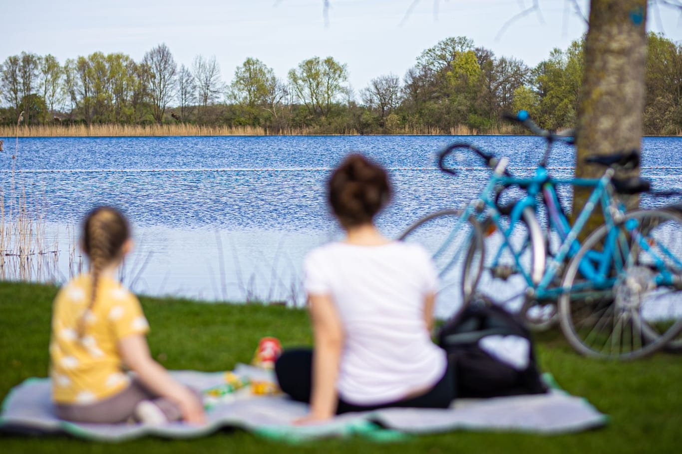 Eine Frau und ein Kind sitzen bei sonnigem Wetter am Ufer des Hufeisensees bei Hannover (Symbolbild): Das Wochenende soll sommerlich werden.