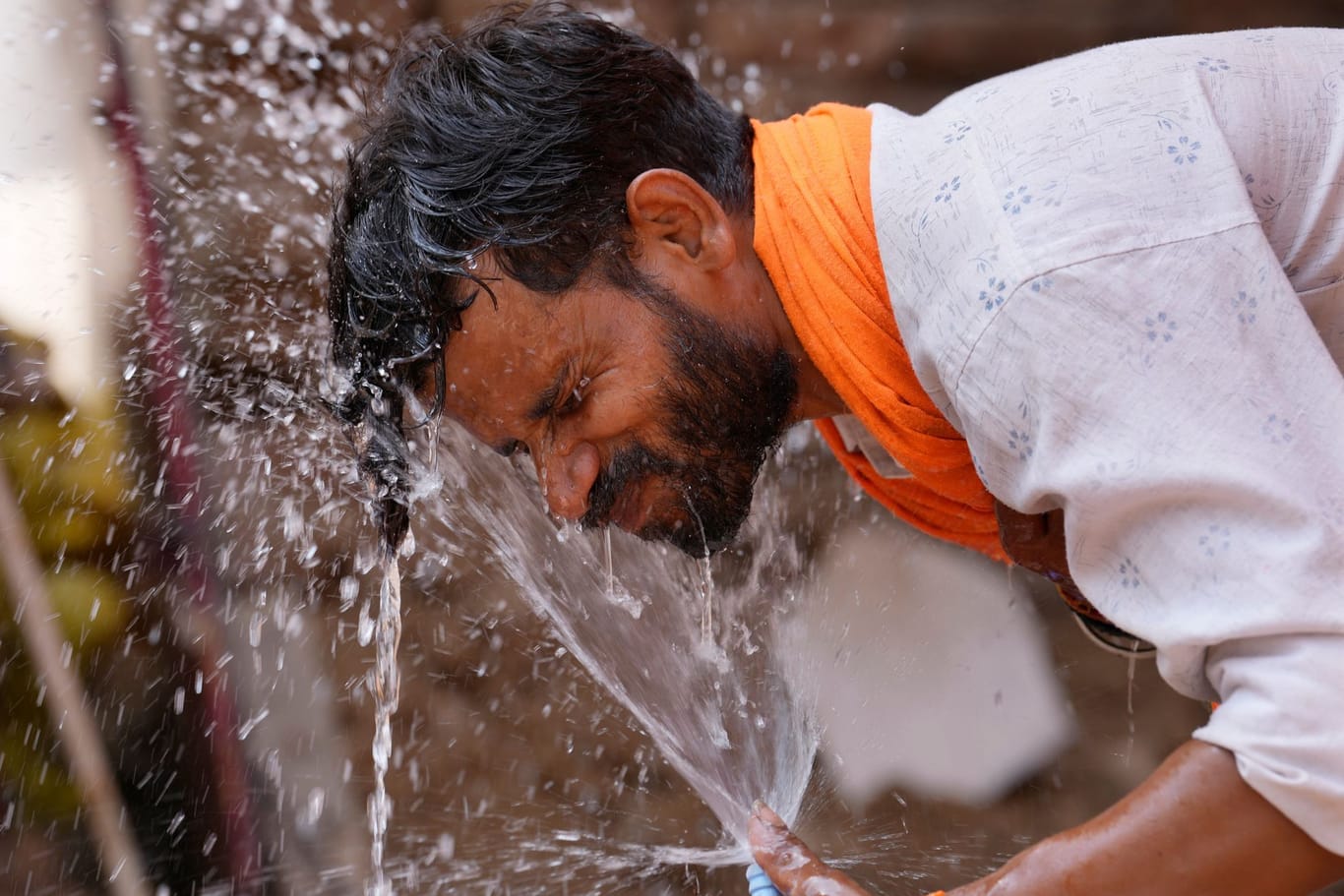Ein Mann spritzt sich Wasser aus einem Wasserhahn am Straßenrand ins Gesicht, um sich an einem heißen Sommertag abzukühlen.