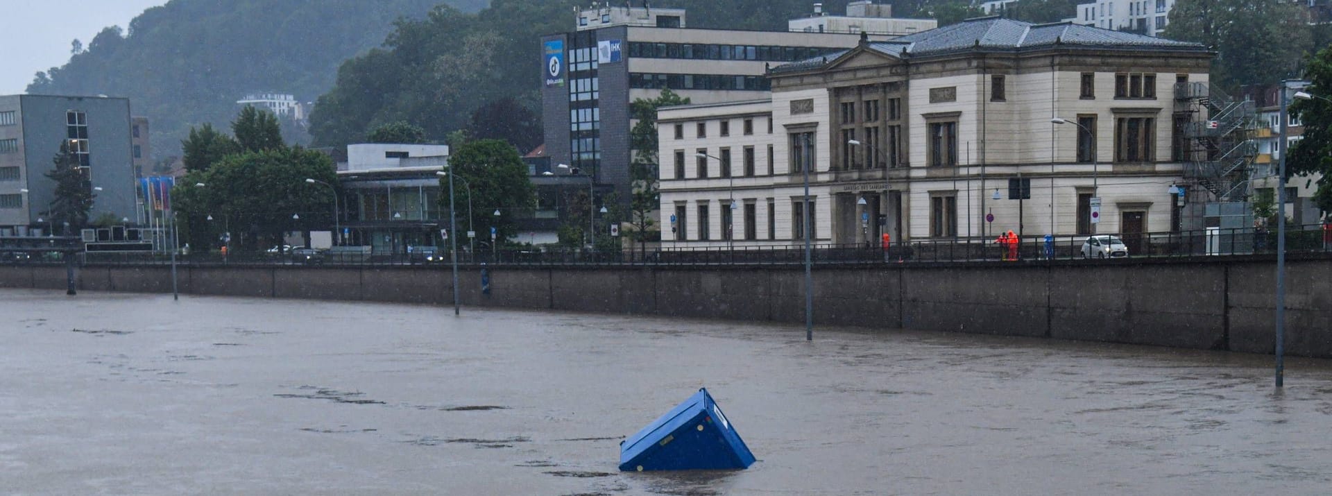 Die Wassermassen haben Baucontainer mitgerissen. Diese schwimmen als Treibgut am saarländischen Landtag vorbei.