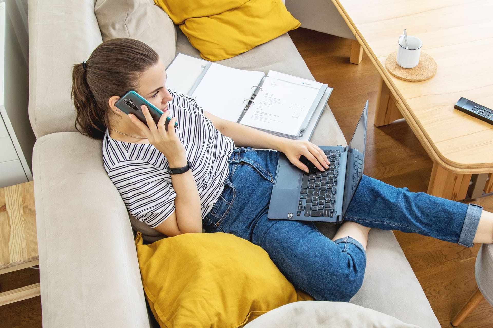 Eine Frau mit Telefon und Laptop auf einem Sofa