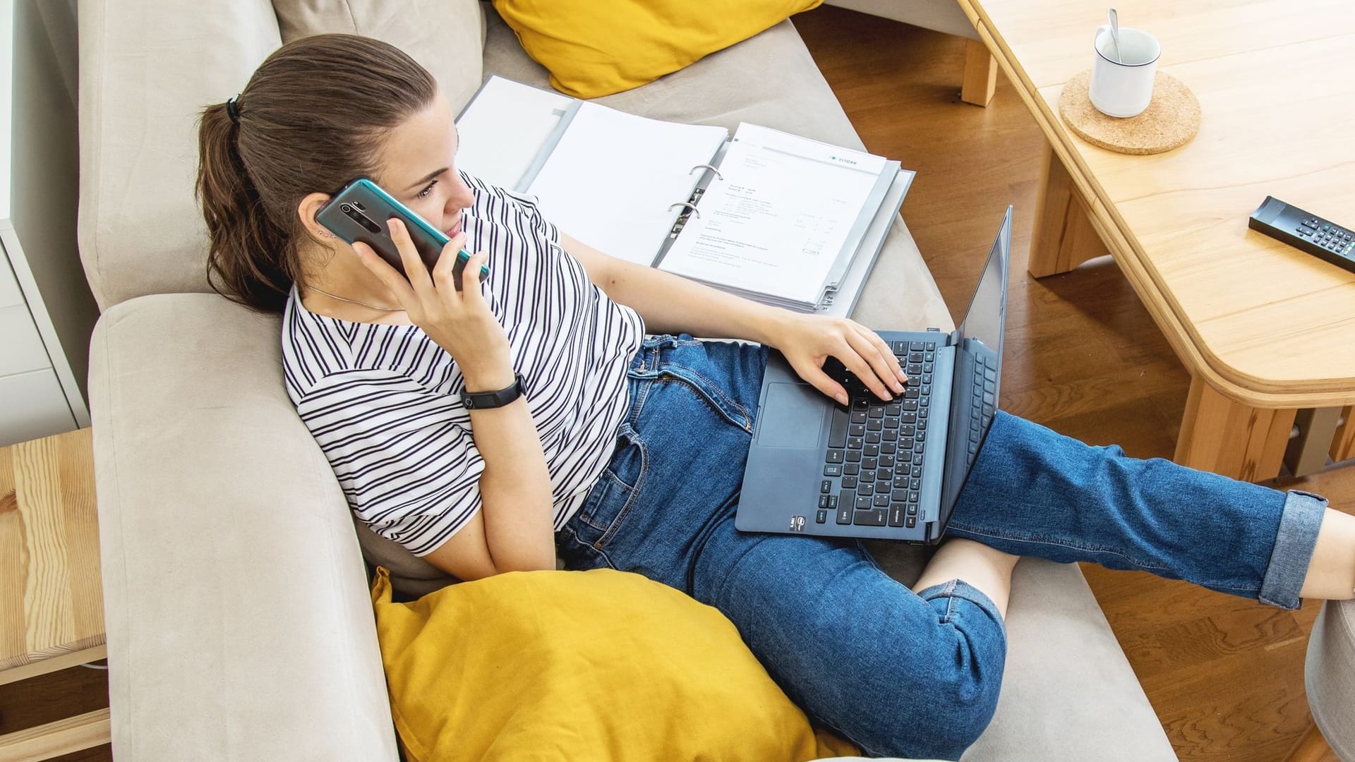 Eine Frau mit Telefon und Laptop auf einem Sofa