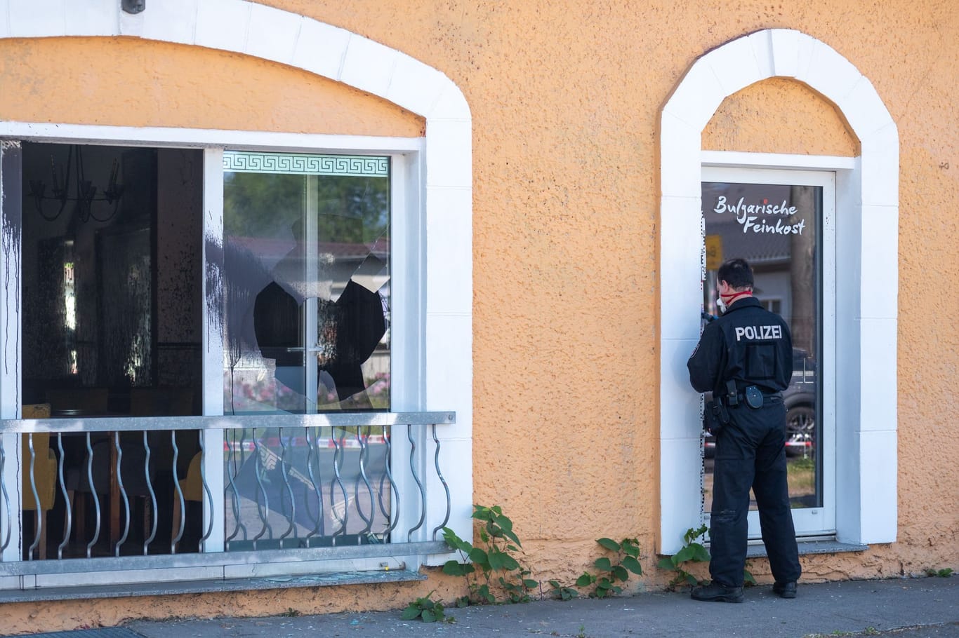 Ein Polizist sichert an einer Tür von einem Restaurant in Hoppegarten Spuren: In dem Restaurant wurde eine Scheibe eingeschlagen, die Fassade beschmiert und Buttersäure verteilt.