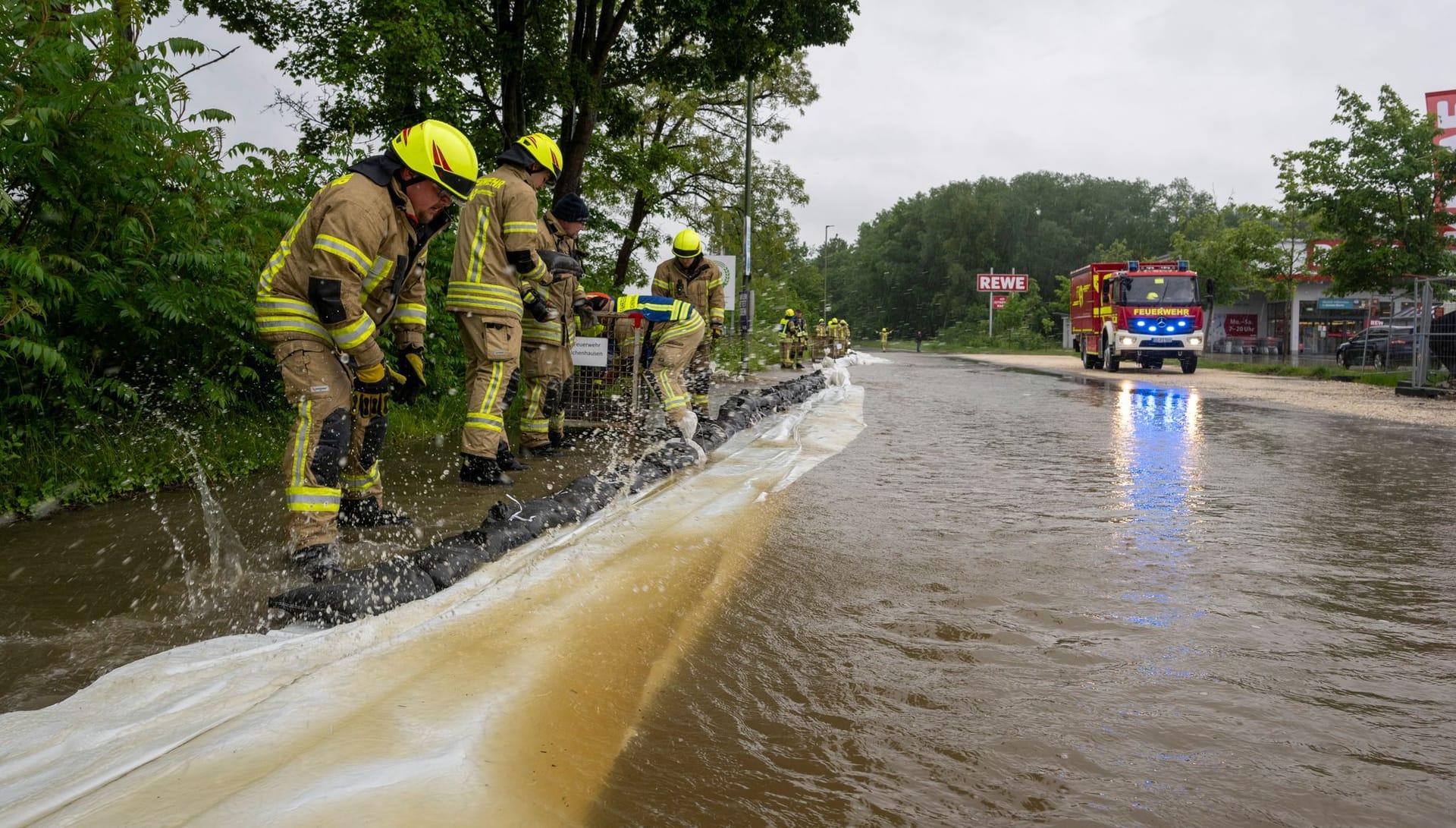 Feuerwehrleute arbeiten an einer von der Günz überfluteten Straße in Ichenhausen, um das Wasser aus der Stadt fernzuhalten.