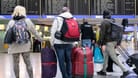 Der Frankfurter Flughafen (Archivbild): Passagiere stehen mit ihren Koffern vor einer Anzeigetafel im Flughafen.