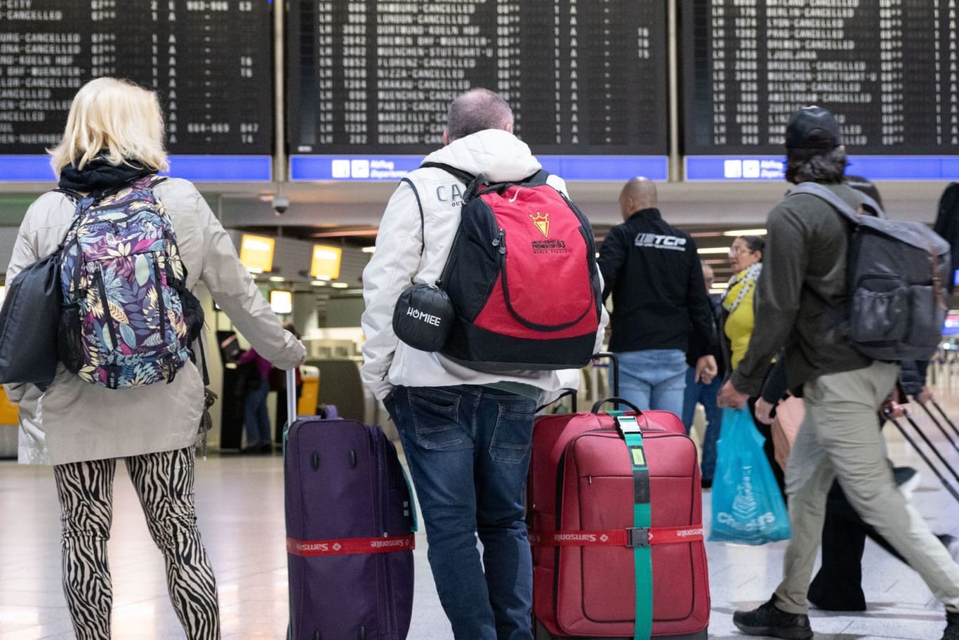 Der Frankfurter Flughafen (Archivbild): Passagiere stehen mit ihren Koffern vor einer Anzeigetafel im Flughafen.