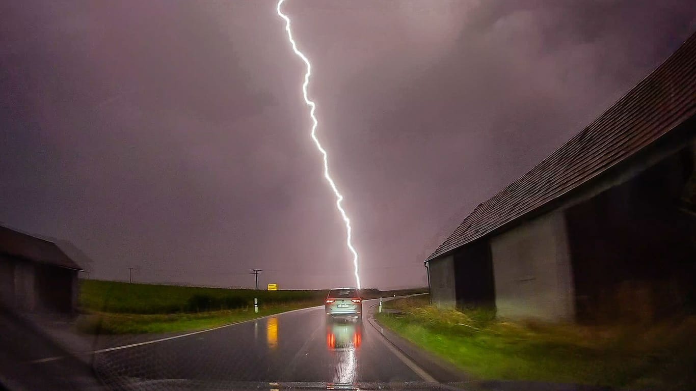 Ein Blitz ist am Himmel hinter einer Straße zu sehen. Schwere Unwetter haben auch am Donnerstagabend noch zu Überflutungen geführt.