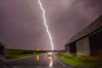 Ein Blitz ist am Himmel hinter einer Straße zu sehen. Schwere Unwetter haben auch am Donnerstagabend noch zu Überflutungen geführt.