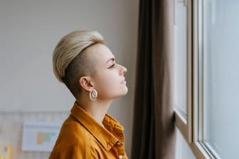 Eine junge Frau guckt nachdenklich aus dem Fenster (Archivbild): Fast die Hälfte aller 16- bis 30-Jährigen fühlt sich einsam in Deutschland.
