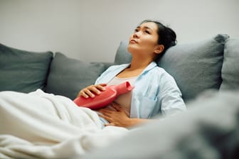 Frau sitzt mit Wärmflasche im Bett