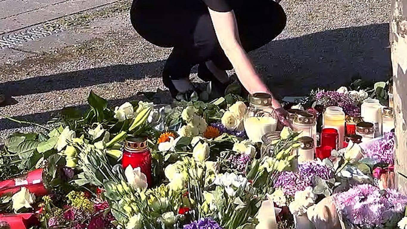 Bad Oeynhausen: Eine Frau stellt eine Kerze neben Blumen, während Menschen nach einem tödlichen Angriff im Kurpark trauern.